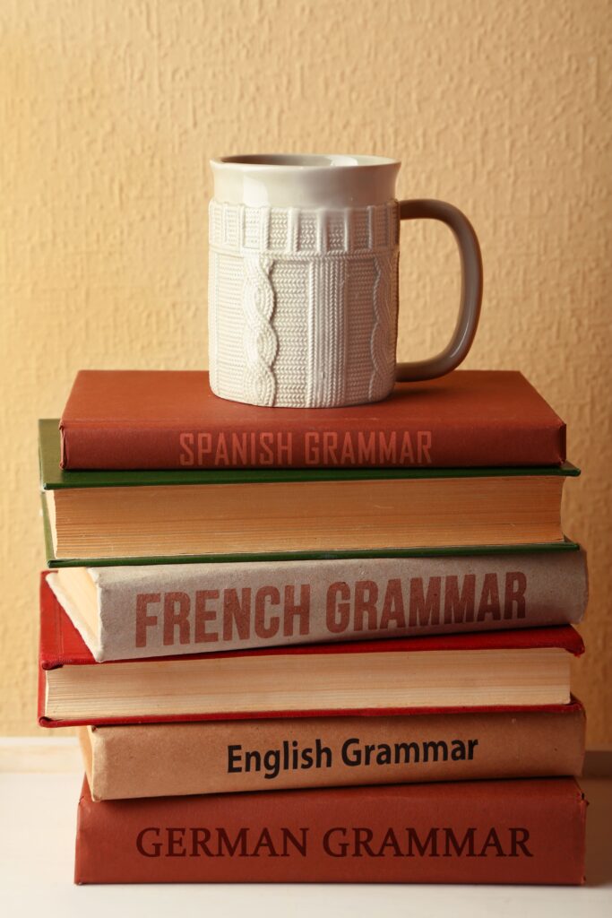 Pile de livres de grammaire de plusieurs langues, notamment française, anglaise et allemande, surmontée d'un mug